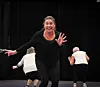 Instruktør i svart leder danse- eller treningsøkt på scene med to eldre deltakere bak