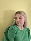 Ung person i grønn bluse ser ned på en undulat som sitter på skulderen foran gul vegg