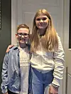 To barn står side om side og smiler foran en hvit dør innendørs