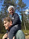 Barn sitter på skuldrene til en voksen på tur i skogen en solrik dag