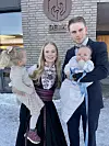 Familie med to små barn poserer foran DELK-bygning på snølagt uteområde.