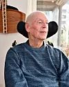 Claes-Göran sitter inomhus i sin rullstol vid ett fönster.