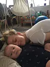 Nicole Ryle ligger på gulvet og hviler kinden mod en baby i et rodet børneværelse.