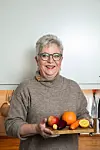 Smilende eldre kvinne på kjøkken holder trefat med frukt og grønnsaker