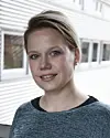 Ung kvinne står utendørs foran lys bygning og ser inn i kameraet