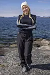Kvinne i friluftsklær står på svaberg foran sjø og fjell i bakgrunnen