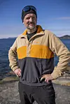 Mann i fargerik Helly Hansen-fleece står ved sjøen på solskinnsdag