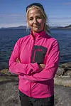 Kvinne i rosa Helly Hansen-jakke står på svaberg foran sjøen.