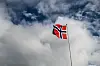 Norsk flagg på flaggstang mot skyet, blå himmel
