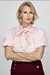 Sanne Gottlieb i lys pink bluse og mørke bukser står med korslagte arme mod lys baggrund.