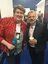 To personer poserer på en messe, med stands i bakgrunnen og en kopp og mikrofon i forgrunnen.