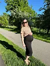 Gravid kvinde med solbriller står på sti i grøn park i solskin