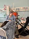 Patient i hospitalseng kigger på barn i barnevogn på stue med medicinsk udstyr.