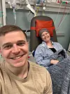 Smilende patient i hospitalsstol og pårørende tager selfie i behandlingsrum