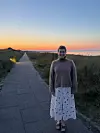 Person står på kyststi ved havet i skumring med farverig solnedgang.