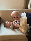 Voksen læner sig ind over baby, der ligger på en lys sofa og smiler