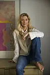 Kvinde sidder afslappet på et møbel foran et farverigt kunstværk i et hjemligt rum.