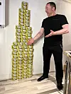 Mann står ved siden av et høyt tårn av små gule esker i et lyst rom.
