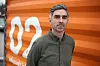 Aleksander Sekowski står foran en oransje reklamevegg med hvitt logoelement.