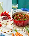 Dessert med bær og nøtter ved siden av en rød gryte med varm mat og grønnsaker.