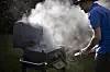 Person ved en røykfylt utendørsgrill med lokket åpent.