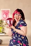 Smilende kvinne med rosa og rødt hår holder en hjerteformet ballong.