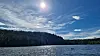 Solfylt innsjø med skogkledd kystlinje, blå himmel og to små båter på vannet.