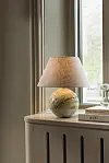 En bordslampa står på en möbel bredvid några staplade böcker vid ett fönster.
