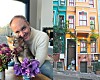 Mann holder en katt ved siden av blomster foran en fargerik bygård.