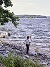 En person står på en stenig strand vid en sjö med vågigt vatten och trädbevuxna öar i fjärran.
