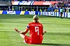 Erling Haaland sitter på gresset og feirer en scoring i Norge mot Irak, med publikum og reklameskilt i bakgrunnen.