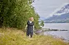 Kvinne går langs gresset ved en innsjø med fjell i bakgrunnen.