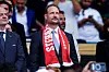 Kronprins Haakon sitter på tribunen med rødt og hvitt skjerf før fotballkampen i Miami.
