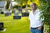 Einar Gelius står ved en gravplass med gravsteiner og grønt gress i bakgrunnen.