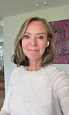 Kvinne tar en selfie innendørs med et fargerikt bilde på veggen bak seg.