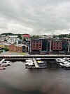 Småbåter ved brygge foran moderne bygg langs en havn under grå himmel.