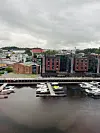 Småbåter ved brygge foran moderne bygg langs en havn under grå himmel.