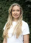 Portrett av en kvinne med langt blondt hår og hvit T-skjorte foran en mørkegrønn bakgrunn.