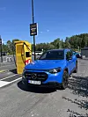 Blå Mercedes-Benz ved gul ladestasjon på en parkeringsplass i sollys.