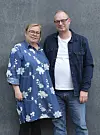 To voksne står tæt sammen foran en grå væg i afslappet tøj