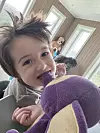 Barn som holder og biter i en lilla kosebamse innendørs.
