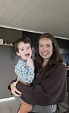 Kvinne holder et smilende lite barn i et moderne kjøkken.