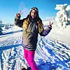 Person i vinterklær står på snø og viser fredstegn mot kamera.