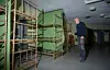 En man står i ett källarliknande rum med metallsängar, gröna väggar och taklampor.