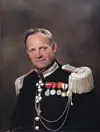 Mann i mørk paradeuniform med medaljer og sølvfargede epåletter foran en mørk bakgrunn.