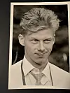 Sort-hvitt portrett av ung mann med lyst hår, hvit skjorte og slips på et papirark.