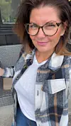 Kvinne med briller og rutete skjorte tar et nært selvportrett utendørs.