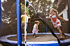 Tre barn leker og hopper på en trampoline med sikkerhetsnett i en hage.