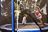 Tre barn leker og hopper på en trampoline med sikkerhetsnett i en hage.