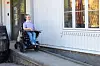 Mari i elektrisk rullestol på en rampe utenfor et hvitt trehus.